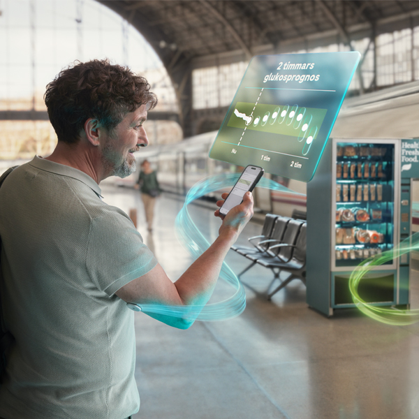 Person kontrollerar sina glukosnivåer på telefonens app, som visar avläsningar och prognosgraf. Kontinuerlig glukossensor diskret fäst på hens arm.
